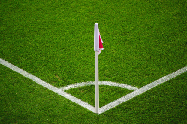 Ein Fußballfeld mit grünem Rasen, weißen Begrenzungslinien und einem weißen Pfosten mit einer roten und weißen Flagge, die den Elfmeterpunkt markiert.