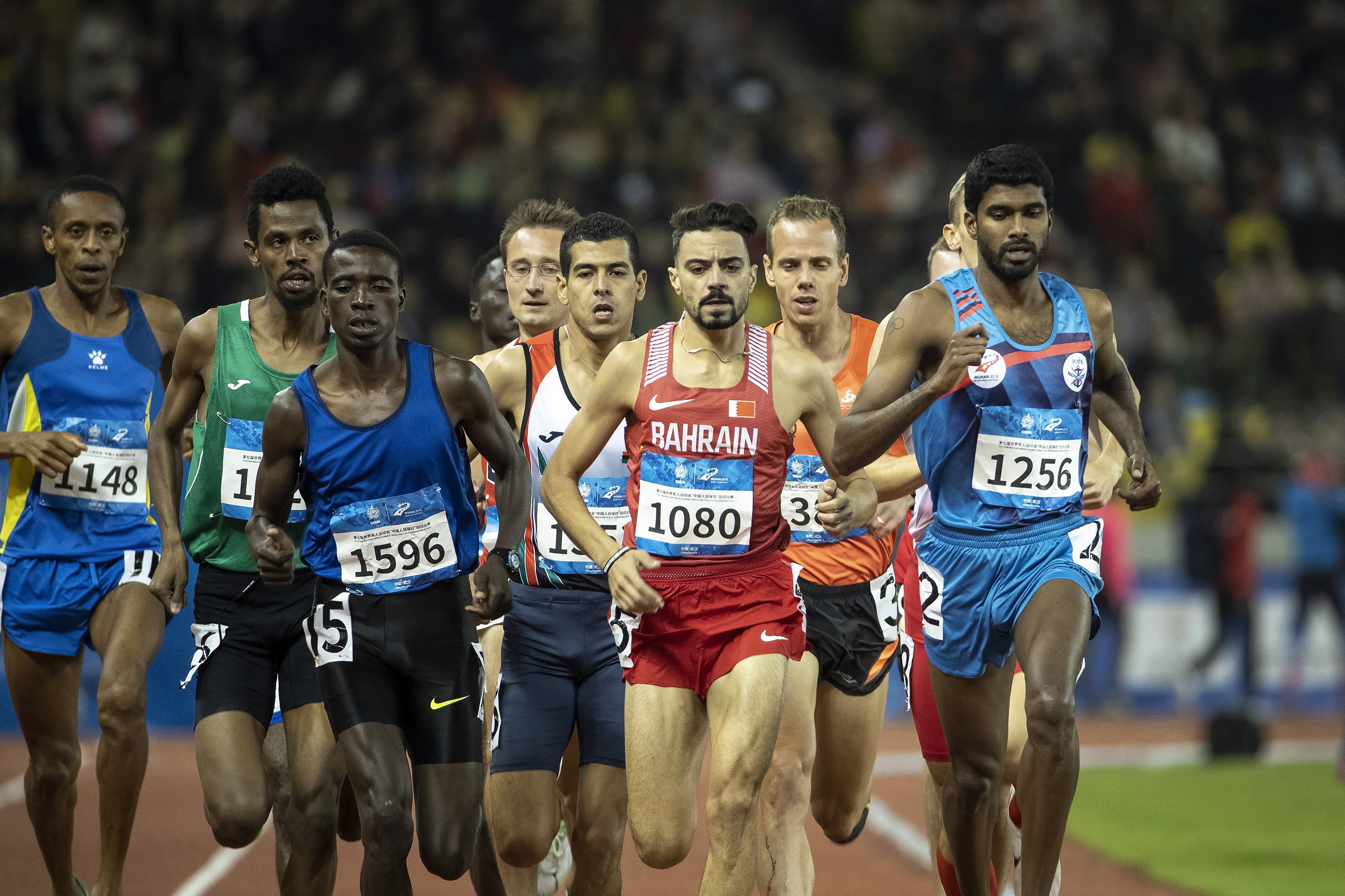 Eine Gruppe von Männern, die auf einer Bahn laufen und an einem Rennen teilnehmen, mit einigen, die zum Ziel sprinten, und einem unscharfen Hintergrund.