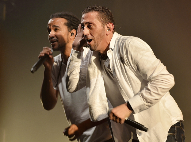 Zwei Männer in legerer Kleidung stehen nebeneinander auf einer Bühne und halten jeweils ein Mikrofon in der Hand.