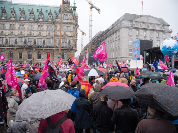 Eine große Gruppe von Menschen nimmt an einer Frauen-Demo in Berlin teil, hölt Schirme, Plakate und Luftballons vor einem Gebäude.
