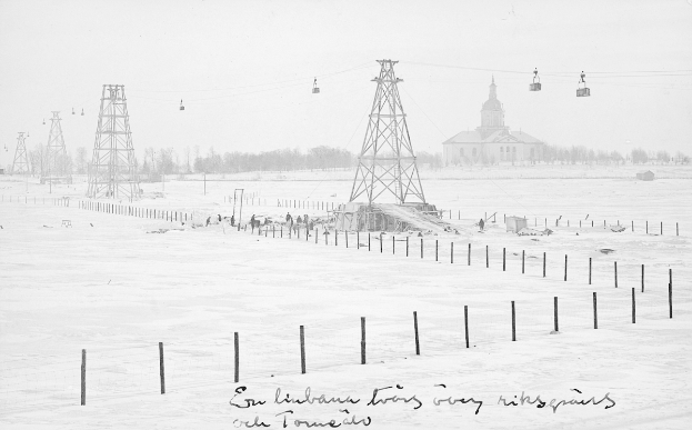 Ein Schwarz-Weiß-Foto eines Skilifts in einer verschneiten Landschaft, umgeben von Pfölen, Dröhnen, Bäumen und einem Gebäude im Hintergrund, mit Text unten.