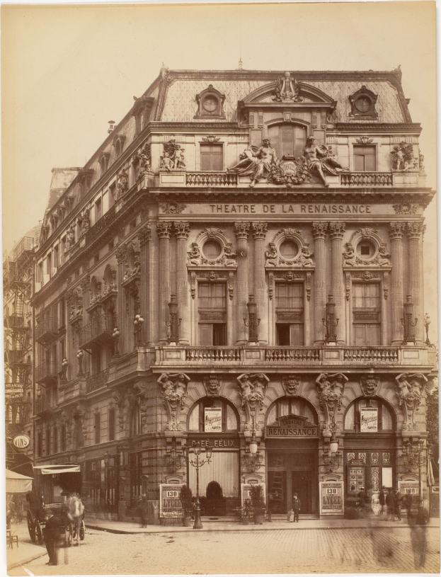 Schwarz-weißes Foto des Théâtre de la Renaissance in Paris mit einer Fassade mit Fenstern, Säulen, Bögen und Skulpturen sowie einer StraßenSzene mit Menschen und Fahrzeugen davor und Himmel darüber.