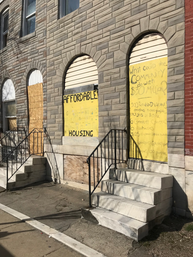 Verschlossenes Gebäude mit "Bezahlbarer Wohnraum"-Schilder, Treppe mit Geländer und Straße unten.