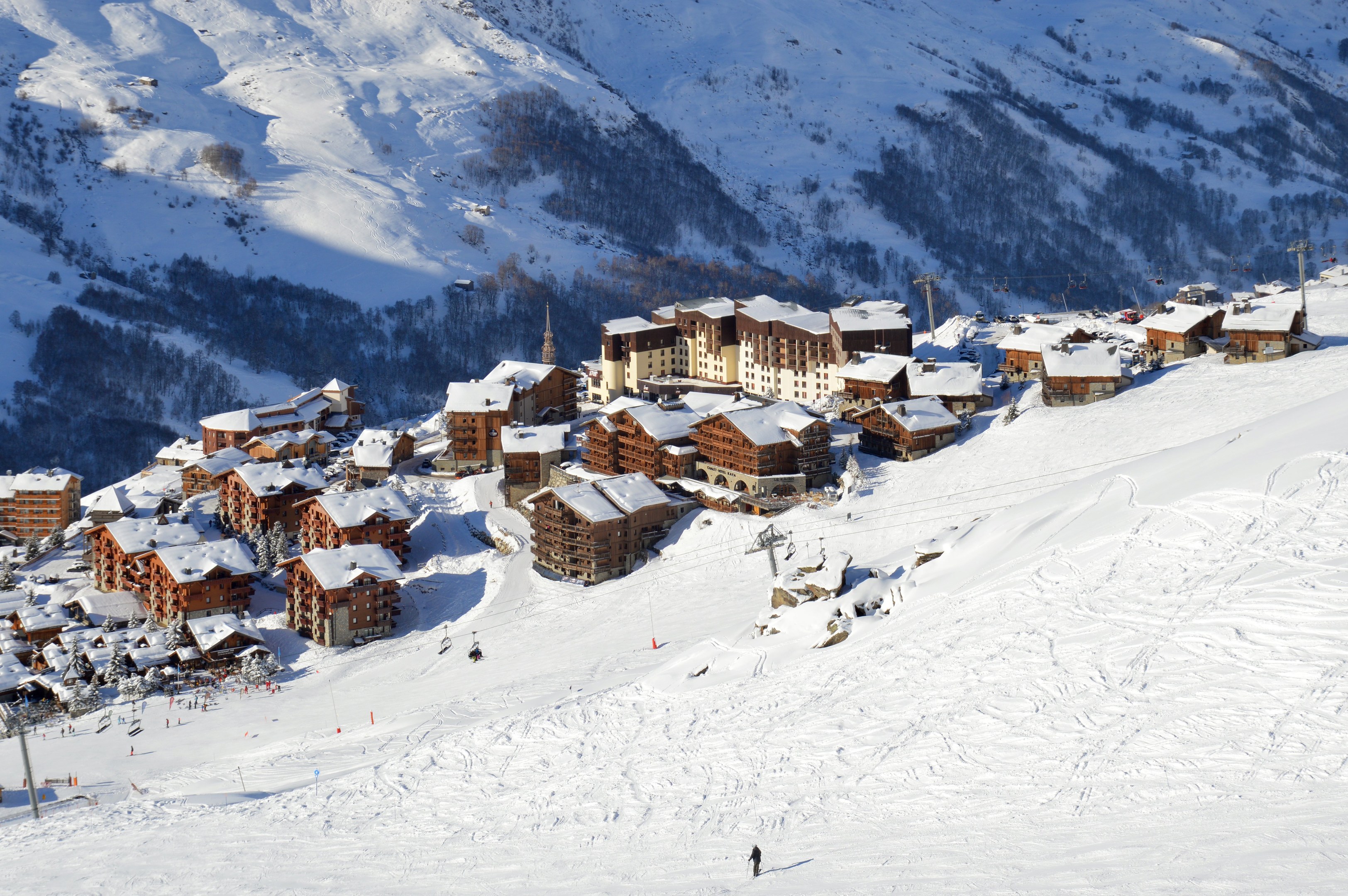 Ein Skigebiet in den französischen Alpen mit schneebedeckten Bergen, Gebäuden, Bäumen und Skifahrern auf den Pisten.