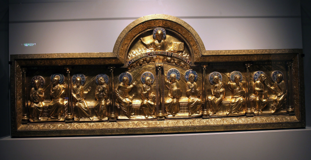 Prunkvoller goldener Rahmen mit detailreichen Skulpturen in einem Museum ausgestellt, vor einer neutralen Wand.