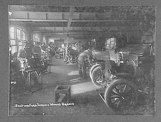 Schwarzes und weißes Foto von Männern bei der Arbeit an einem Auto in einer Ford-Werkstatt mit Fahrzeugen, Werkzeugen und Fenstern