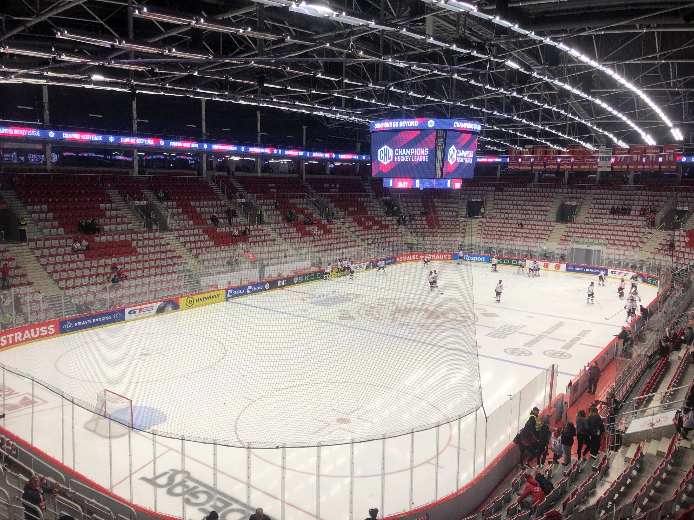Eishockeyspiel in einer großen Arena zwischen den St. Louis Blues und den Detroit Red Wings, mit Zuschauern auf den Sitzplätzen und in der Nähe des Spielfelds stehend, umgeben von einem Zaun und einem Display.