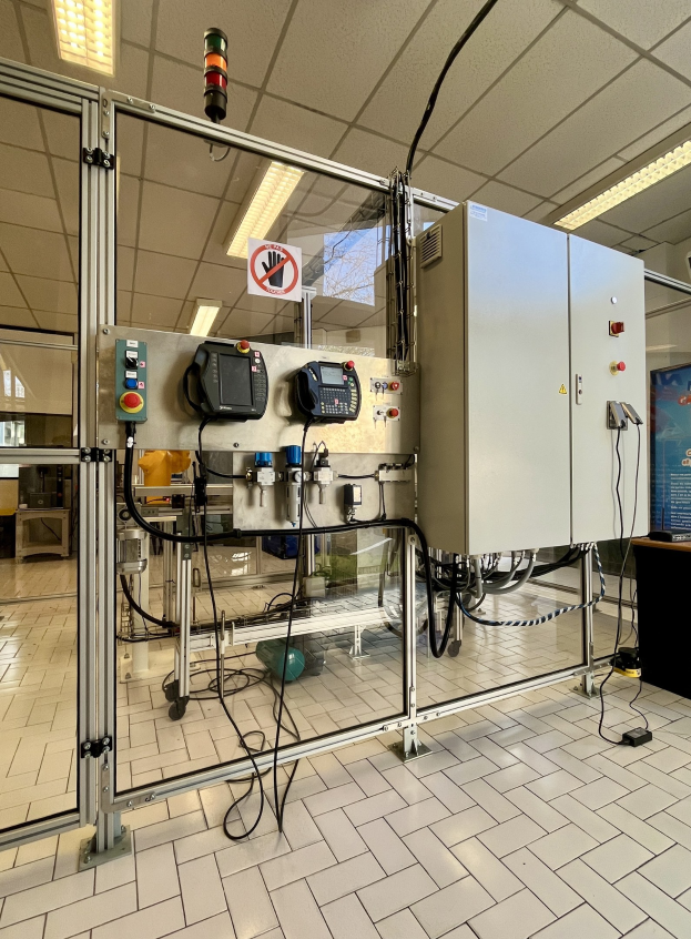 Große industrielle Automatisierungsmaschine in einer Einrichtung mit einer Wand, Deckenleuchten und einer Steuerkonsole auf der rechten Seite.