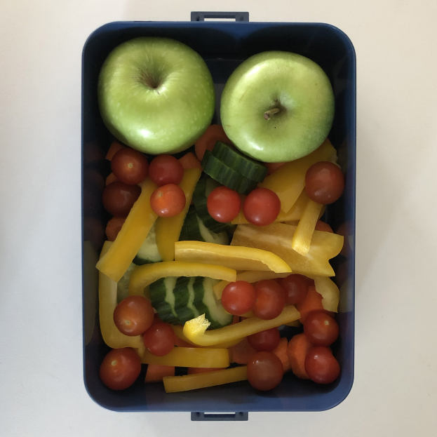 Ein blauer Lunchbox mit zwei grünen Äpfeln, Tomaten, Gurken und anderen Obst und Gemüse.