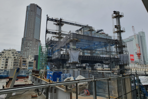 Ein großes Gebäude im Bau in einer Stadt, umgeben von einem Metallzaun, mit benachbarten Gebäuden, Polen, einer Tafel, Fahrzeugen, Drähten und einem bewölkten Himmel.