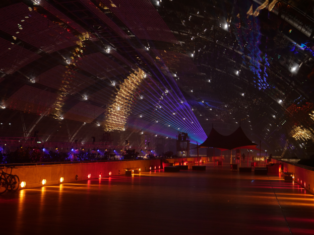 Ein geräumiger Raum mit zahlreichen Deckenlampen, ein Fahrrad auf der linken Seite und einige Menschen im Hintergrund, die eine helle und lebendige Veranstaltungsatmosphäre schaffen.