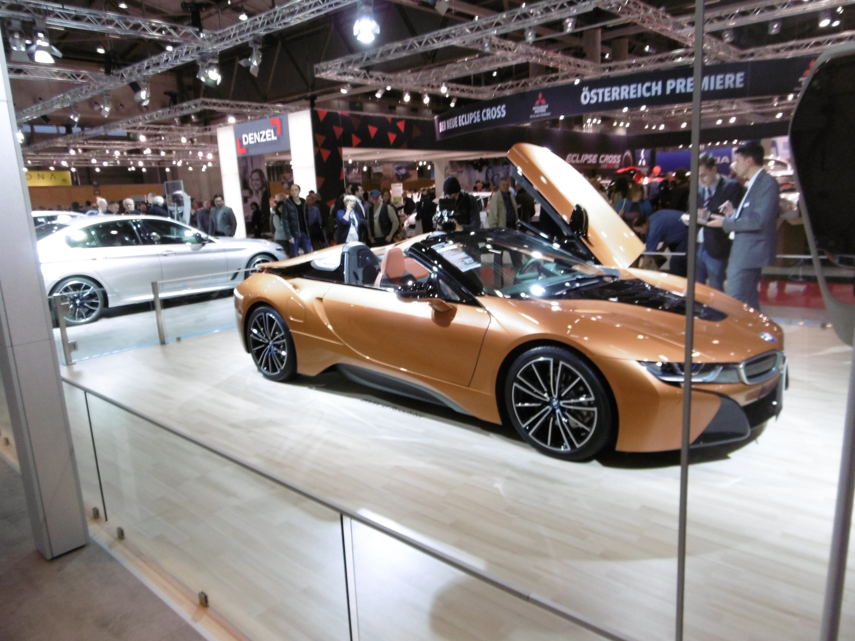 Ein glänzender schwarzer BMW i8 Roadster mit Chromakzenten auf der Frankfurter Motor Show umgeben von formell gekleideten Gästen in einer Atmosphäre der Aufregung.