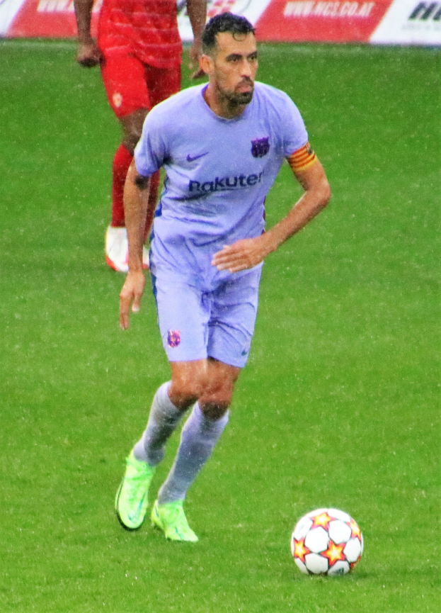 Fußballspieler in Sportbekleidung und -schuhen auf dem Feld mit einer Texttafel im Hintergrund.