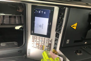 Ein Nahaufnahme eines Geräts mit Touchscreen, Knöpfen und einer Glasfenster, das das Innere eines Fahrzeugs zeigt.