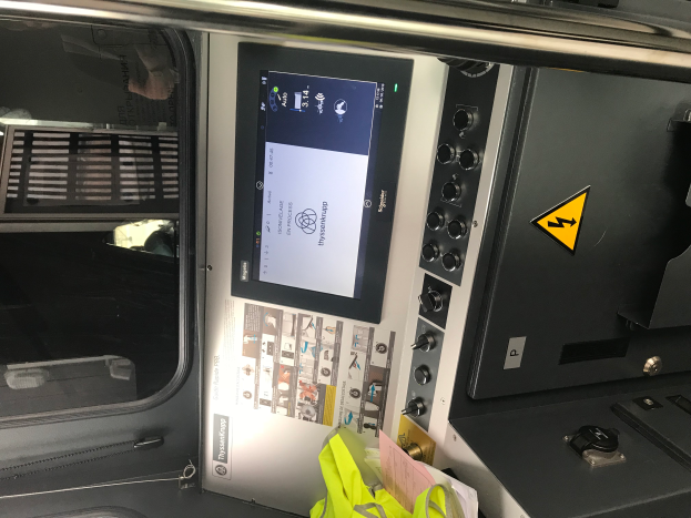 Ein Nahaufnahme eines Geräts mit Touchscreen, Knöpfen und einer Glasfenster, das das Innere eines Fahrzeugs zeigt.