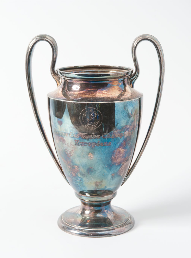 Der UEFA-Champions-League-Pokal, ein stählerner Pokal mit zwei Griffen und einem blauen und silbernen Farbschema, der mit 'UEFA Champions League' auf einem weißen Hintergrund eingraviert ist.