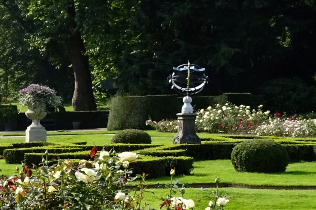 Ein Garten in den Königlichen Botanischen Gärten Edinburgh mit verschiedenen Pflanzen, Blumen, Gras, Bäumen und einer zentralen Statue.