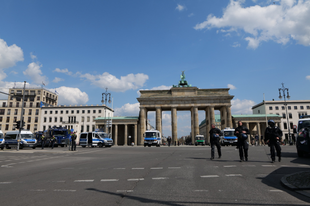 Gruppe von Polizisten vor dem Brandenburger Tor in Berlin, Deutschland, mit Säulen, Statue, umgeben von Gebäuden, Fahrzeugen, Laternen, Verkehrszeichen und bewölktem Himmel.