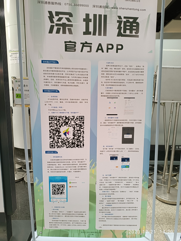 Banner mit einem QR-Code vor einem Gebäude, wahrscheinlich für den Shenzhen International Airport beworben, umgeben von Ständen und Tafeln.