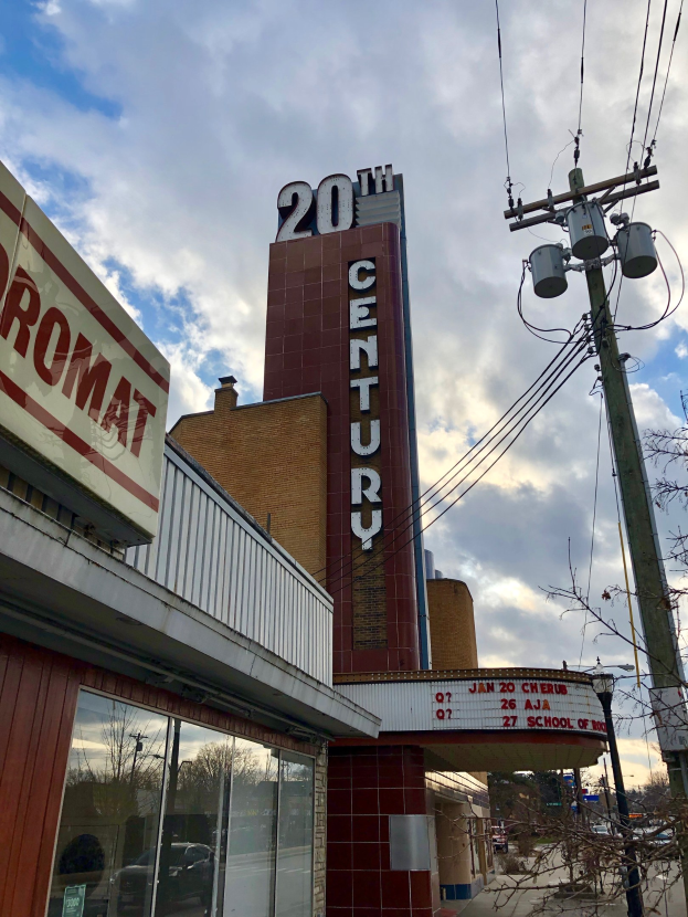 Außenansicht des 20. Jahrhundert Theaters in Detroit, Michigan, mit Glaswänden, Namensschildern, umgeben von Bäumen und Strommasten mit Drähten unter einem bewölkten Himmel.