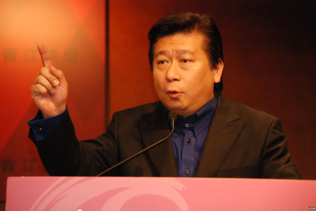 Ein Mann in Anzug und Krawatte, der auf einem Podium vor einem Mikrofon spricht und wie ein politischer Wissenschaftler mit ernster Miene wirkt.