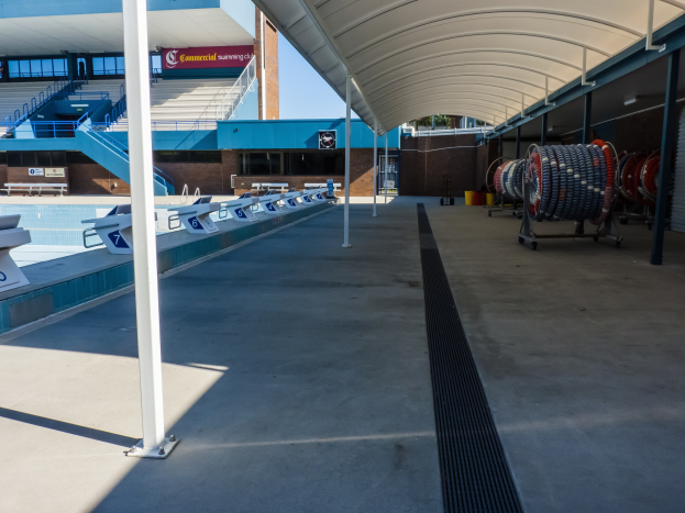 Großes Hallenbad mit zahlreichen Stühlen auf der rechten Seite, Pfählen auf der linken Seite und einem Gebäude mit Treppen, Geländern und Texttafeln im Hintergrund an der University of Texas at Austin.