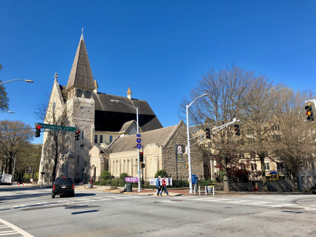 Große Kirche mit Turm an der Straßenecke, beschriftet als St. Lukes Episcopal Church, umgeben von Gebäuden und städtischen Elementen unter einem klaren blauen Himmel.