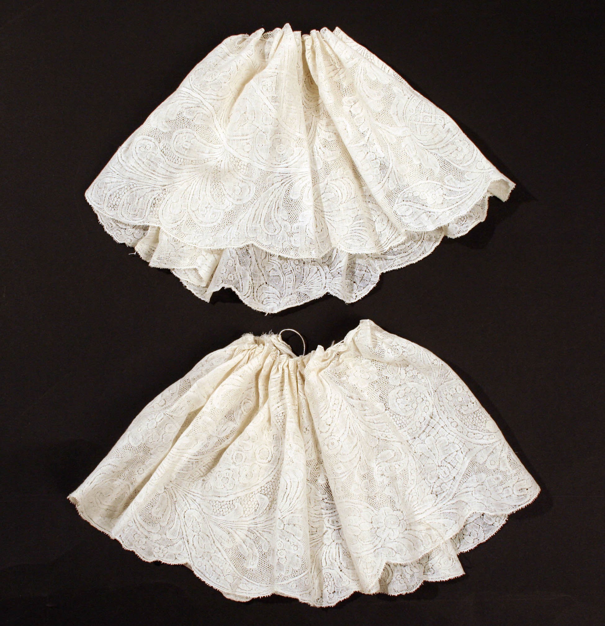 Zwei weiße Spitzenröcke mit zarten Mustern auf schwarzem Hintergrund.