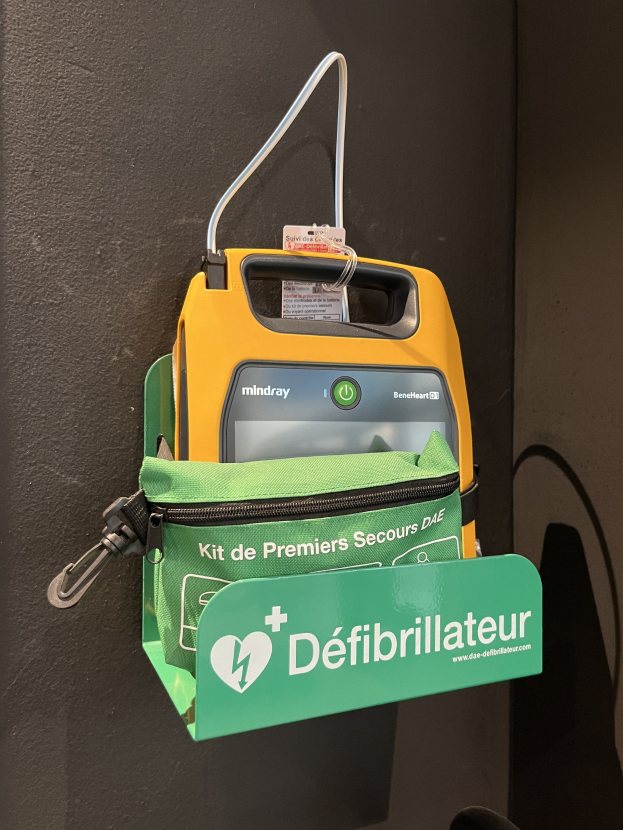 Ein gelb-grüner Defibrillator auf einem schwarzen Tisch neben einer grünen Tasche mit Text zur Angabe von Marke und Modell.