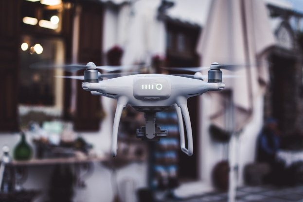 Weißer DJI Phantom 3 Advanced Drohne, die gegen einen unscharfen Hintergrund von Gebäuden und Lichtern fliegt.