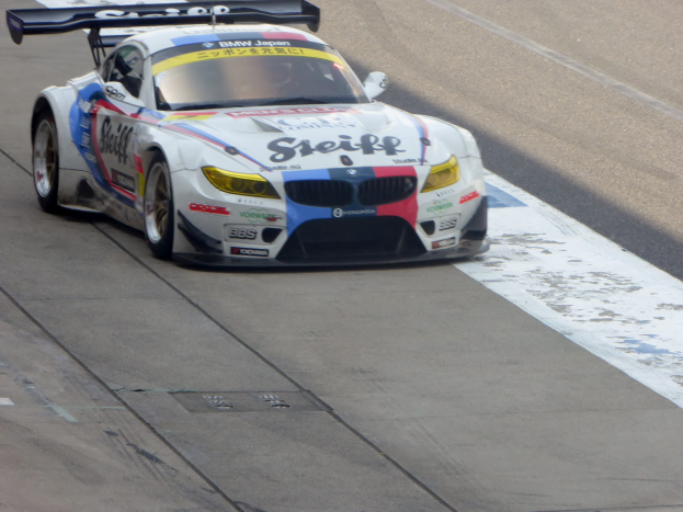 Ein strahlend blauer und weißer BMW Z4 GT3 Rennauto mit großen glänzenden Rädern fährt auf einer Rennstrecke und präsentiert sein aerodynamisches, niedriges Design.