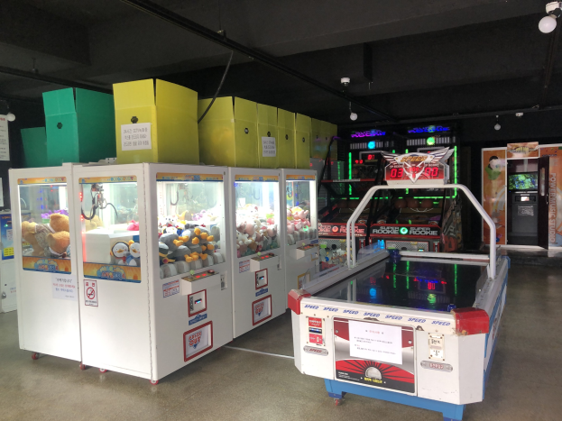 Ein Raum voller verschiedener Arcade-Spiele, mit einem Spielautomaten auf der rechten Seite, einem sichtbaren Boden und Deckenlampen darüber.