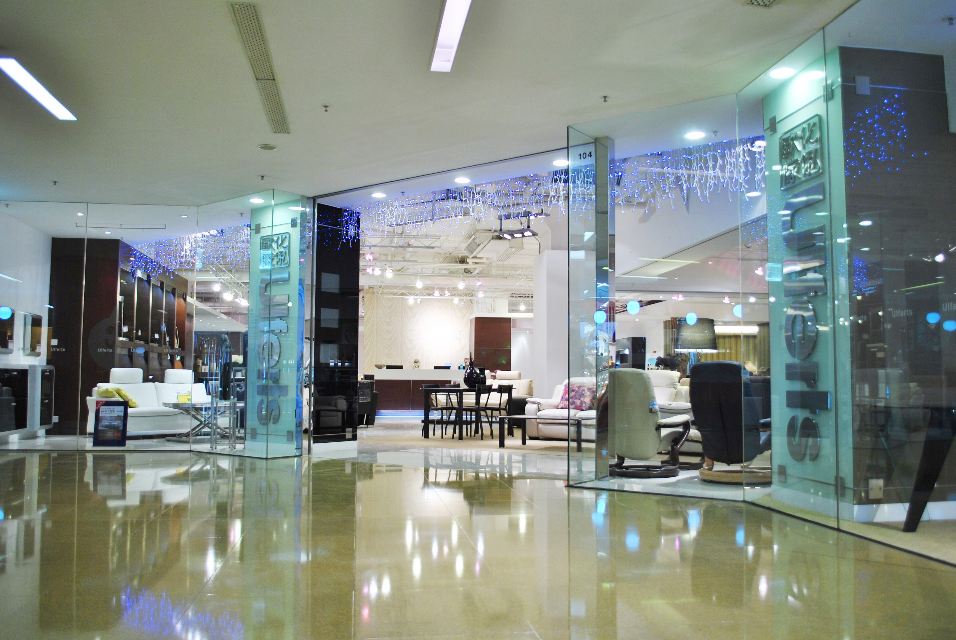 Innenansicht eines möbelgefüllten Ladens mit Stühlen, Sofas, Tischen und anderen Gegenständen, mit sichtbarem Boden und Deckenlicht sowie einem Friseursalon-Schild im Hintergrund.