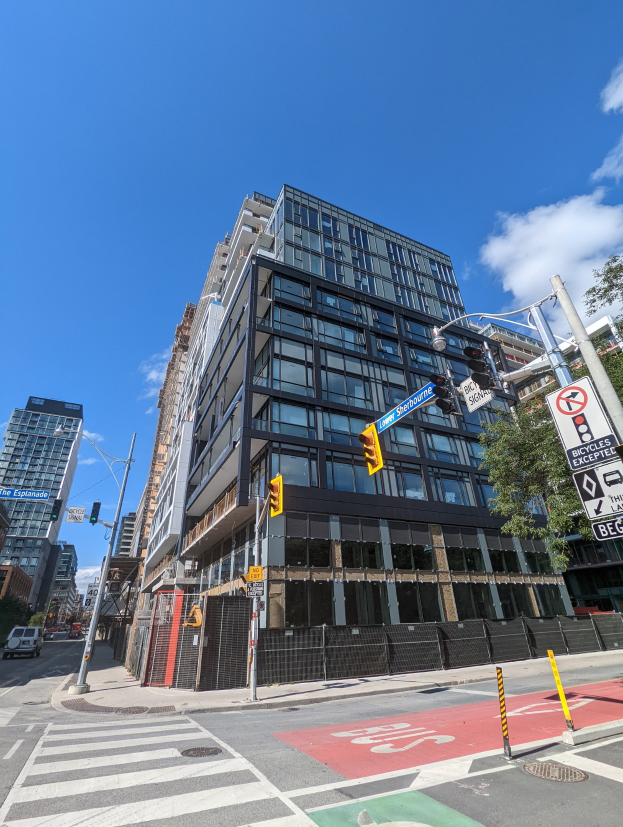 Eine belebte Stadtstraße mit einem hohen Apartment-/Reihenhaus im Hintergrund an der 541 East 57th Street, Unit 541, mit Fahrzeugen, Verkehrsampeln, Schildern, Bäumen und einem Zaun unter einem bewölkten Himmel.