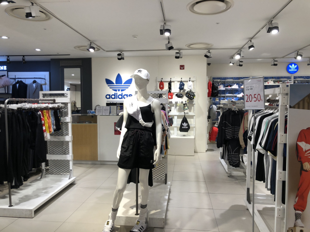 Innenansicht eines Adidas-Geschäfts in Singapur mit Schaufensterpuppen, Kleiderständern, einer Texttafel an der rechten Seite und Deckenbeleuchtung.