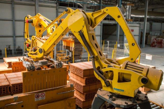 Ein großes Lagerhaus voller numerous boxes, Kräne und diverser industrieller Ausrüstung, mit einem Zaun und Pfählen im Vordergrund und einer Wand im Hintergrund.