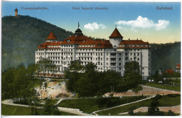 Alte Postkarte des Hotel Imperial in Karlsbad, Deutschland, zeigt ein großes Gebäude mit Fenstern, umgeben von Bäumen, Pflanzen, Gras, einem Pfad, einer Baumgruppe, Hügeln und einem bewölkten Himmel, mit Text oben.