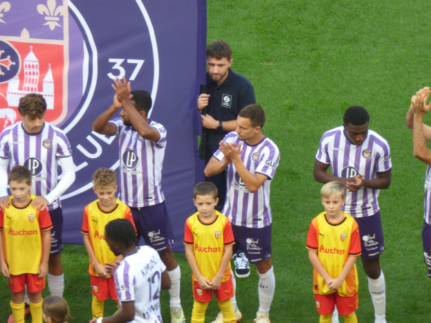 Junge Jungs auf einem Füßtballfeld, die klatschen, mit einem Banner und Logos im Hintergrund auf grüner Wiese.