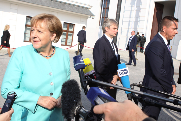 Bundeskanzlerin Angela Merkel bei einer Pressekonferenz im Kanzleramt in Berlin umgeben von Menschen mit Mikrofonen und Gebäuden im Hintergrund.