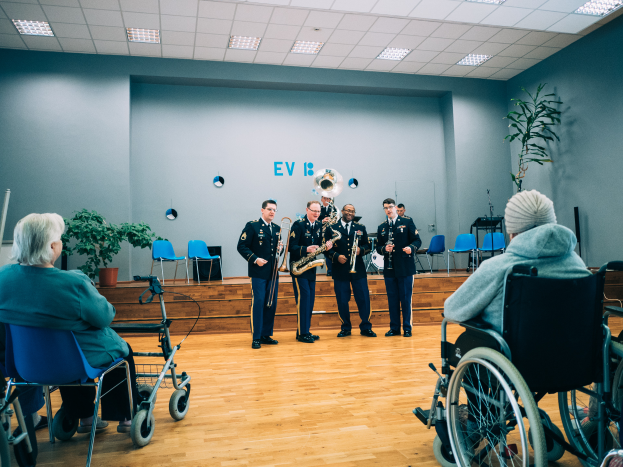Eine Gruppe von Menschen im Rollstuhl, die in einem Raum mit Stühlen, Pflanzen und Deckenleuchten Musikinstrumente spielen.