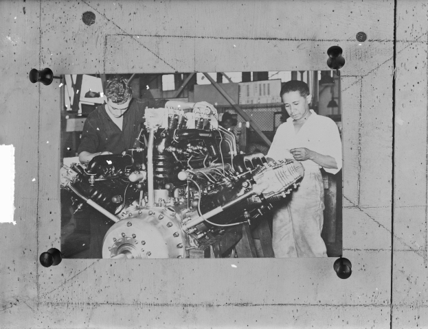 Zwei Männer in einer Fabrik untersuchen ein großes Flugzeugtriebwerk in Schwarz-Weiß.