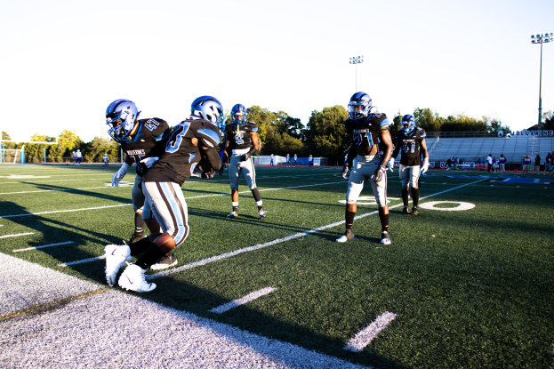 Gruppe von Menschen, die Fußball auf einem Feld mit Bäumen, Laternenmasten und einem klaren blauen Himmel spielen, einige tragen Helme und Schuhe während eines Spiels.