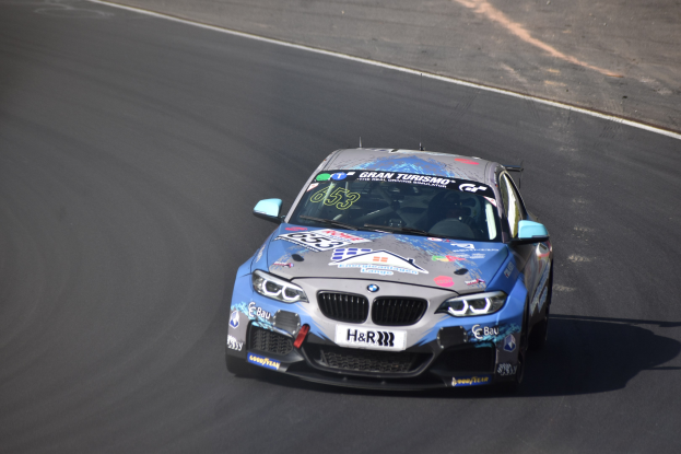 Ein BMW M2 GT3 Rennwagen fährt auf einer Rennstrecke mit Text und Zahlen auf seiner Karosserie.