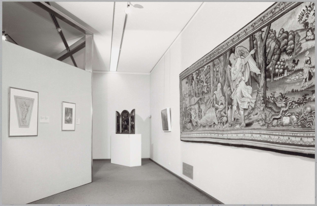 Schwarzes und weißes Foto eines Museumsraums mit einem großen Wandteppich, gerahmten Kunstwerken an den Wänden, Sockelobjekten, Deckenleuchten und dem Text "Museum of Fine Arts, New York City" unten.