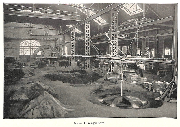 Schwarzes und weißes Foto einer Fabrikhalle mit Arbeitern, die Maschinen bedienen, umgeben von Metallstangen und -rohren, beschriftet mit "Neue Eisengießerei, die erste Fabrik Deutschlands" unten.