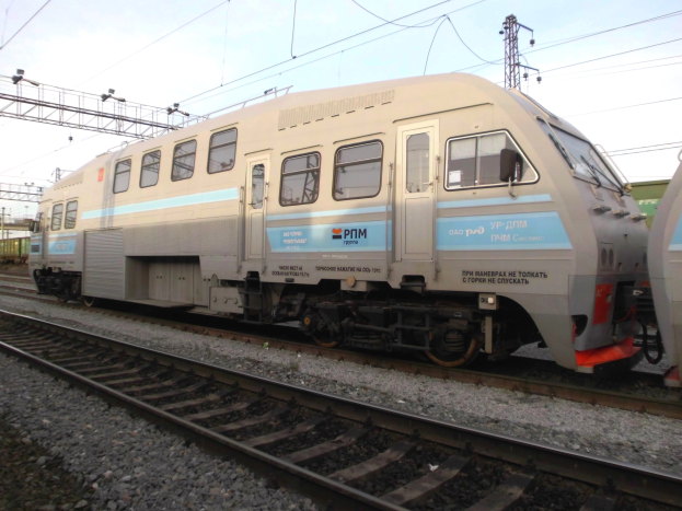 Diesellokomotive auf Schienen neben einem anderen Zug mit Strommasten und Kabeln im Hintergrund und einem klaren blauen Himmel.