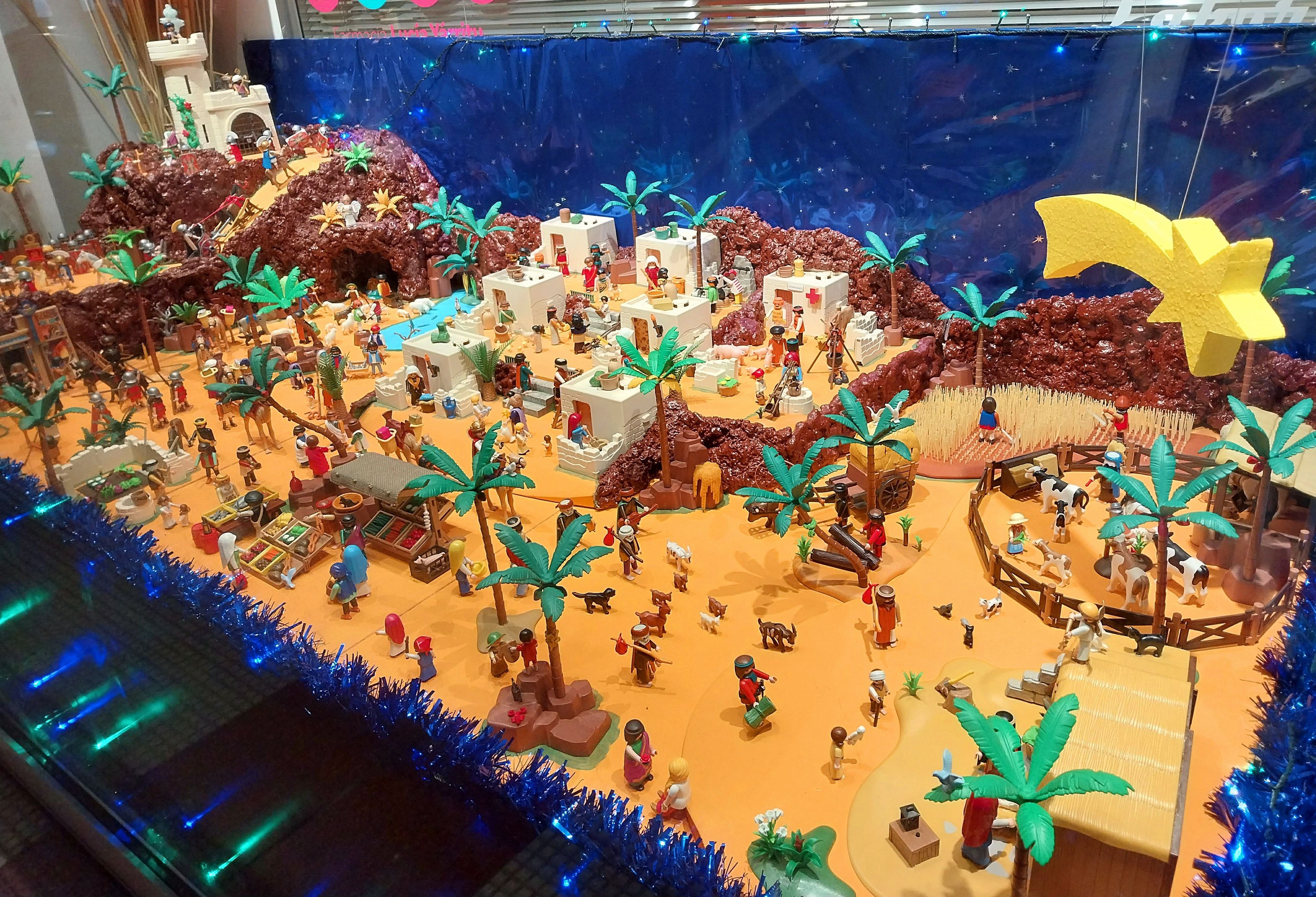 Vitrine voller verschiedener Lego-Steine und -Teile auf einem Tisch, umgeben von Spielzeugen und dekorativen Elementen, mit beleuchteter Wand im Hintergrund.