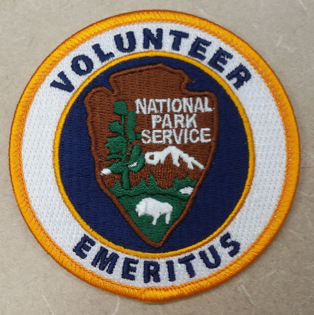 Runder Flicken mit blauem Rand und weißem Hintergrund, der den schwarzen Text 'Volunteer National Park Service Emeritus' in der Mitte eines gelben Kreises zeigt.