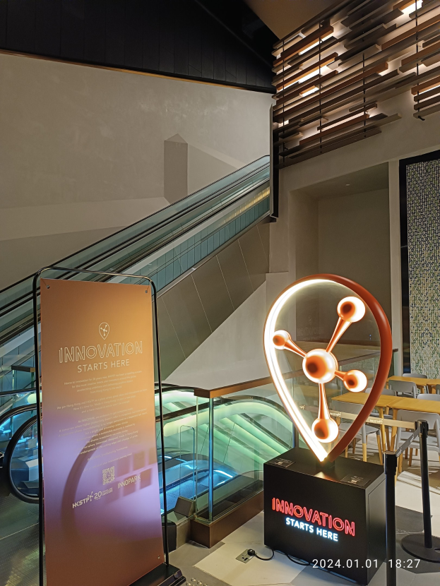 Großes Schild mit der Aufschrift "Innovation beginnt hier" in einem Gebäude mit einer Treppe im Hintergrund, Tischen und Stühlen auf der rechten Seite und einem Expo-Schild auf der linken Seite.