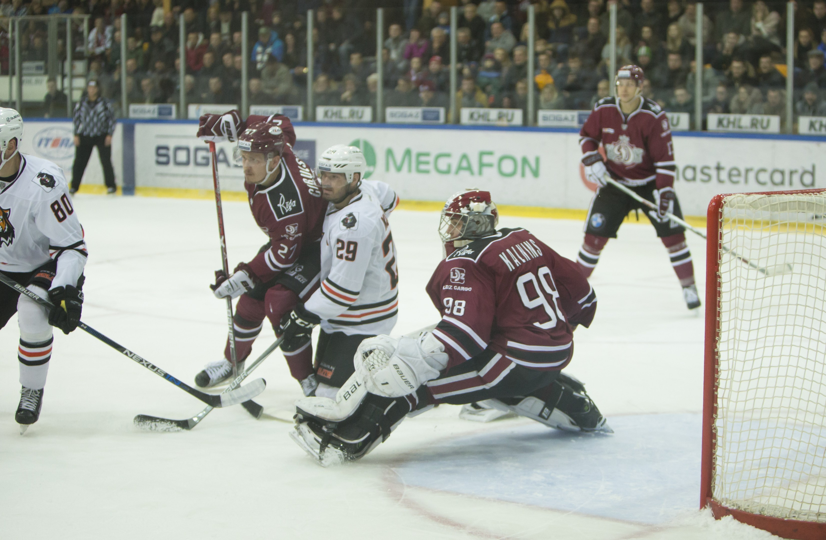 Gruppe von Menschen in Helmen und Hockey-Ausrüstung auf einem Eisstadion mit einem Tor auf der rechten Seite, Zuschauern auf den Tribünen und Bannern im Hintergrund.